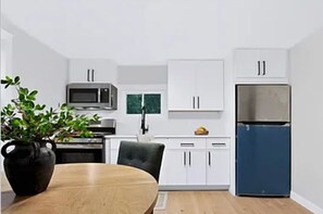 A modern kitchen with white cabinets, a microwave, a refrigerator, and a dining table with a plant.