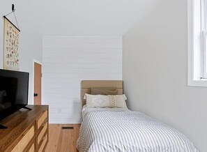 Ein Schlafzimmer mit Bett, Kommode, Fernseher und Fenster.