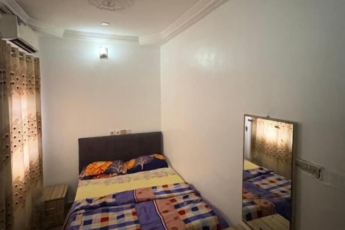 Quarto com cama, mesa de cabeceira, espelho e luminária na parede.
