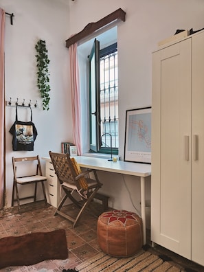 Une pièce avec un bureau blanc, deux chaises, une plante suspendue, une fenêtre donnant sur un beau paysage et un meuble.