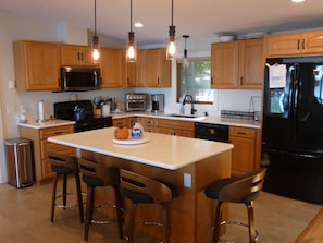 A modern kitchen with wooden cabinets, stainless steel appliances, and a central island with bar stools. - Barefoot Shores at Torch Lake (Rapid City)