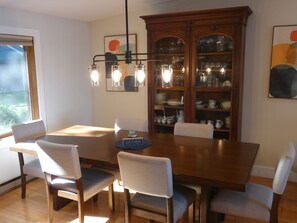 Ein Esszimmer mit Holztisch, sechs Stühlen, einer Chandelierleuchtre und einer Vitrine mit Geschirr.
