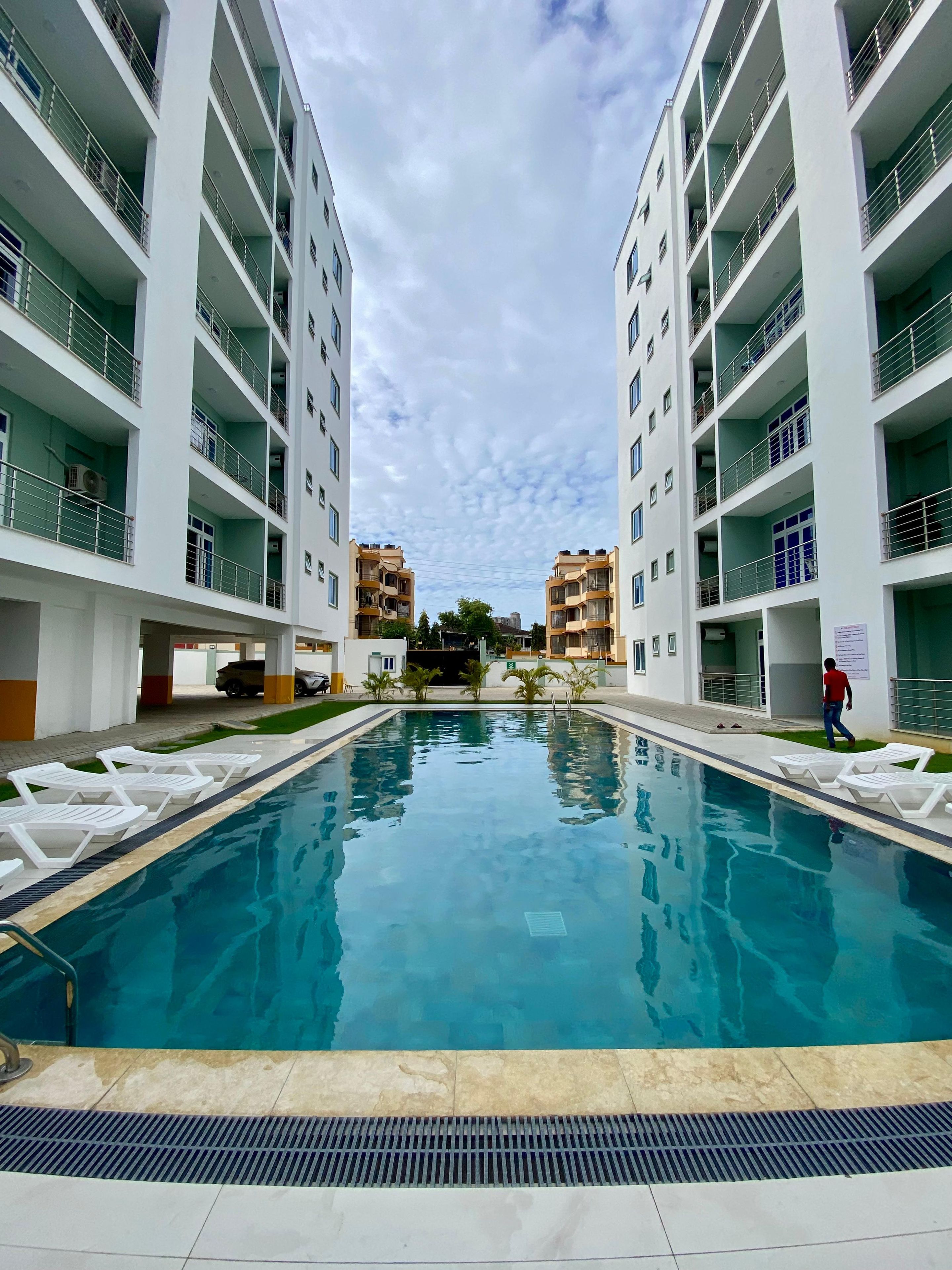 Une piscine entourée de chaises longues, elle-même bordée d’immeubles à plusieurs étages dotés de balcons.