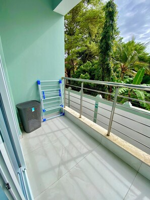 A balcony with a metal railing, a black trash bin, and a view of lush greenery. -  2BR Coastal Getaway Near Nyali Beach — your cozy home away from home! (Mombasa)