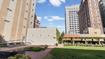 Un patio con mesas al aire libre, un jardín y edificios al fondo.