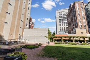 Un patio con mesas al aire libre, un jardín y edificios al fondo.