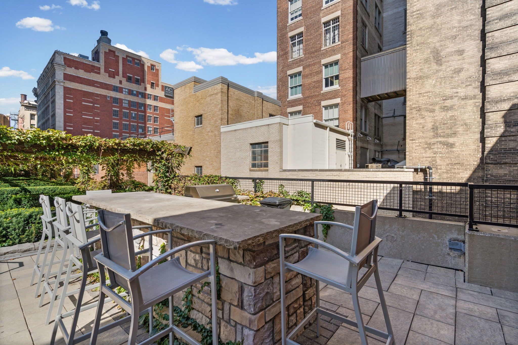 An outdoor patio with a stone table and metal chairs, surrounded by a brick wall and greenery.