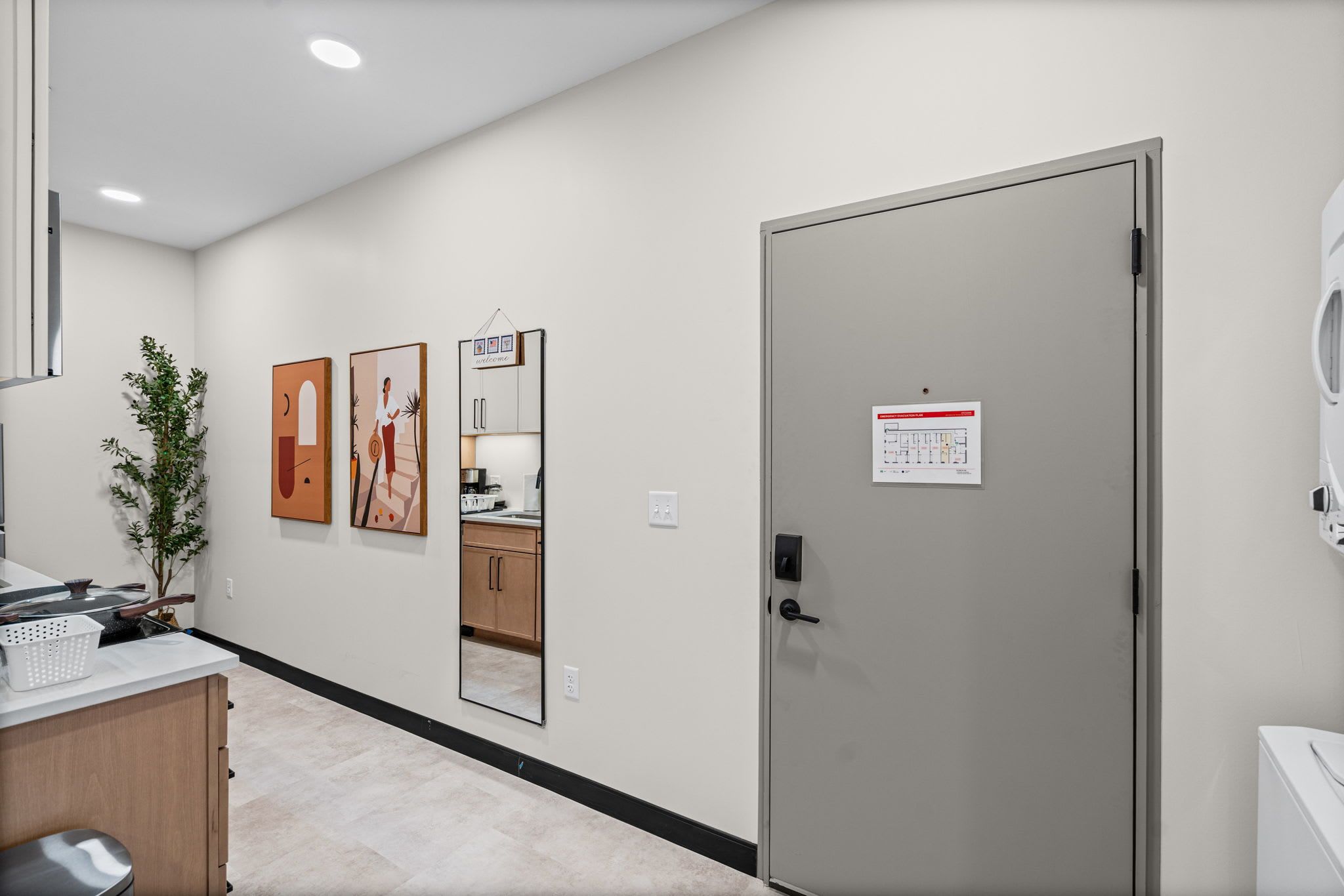 A hotel room with a kitchenette, a door with a sign, and artwork on the wall.