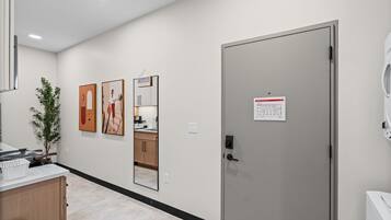 A hotel room with a kitchenette, a door with a sign, and artwork on the wall.