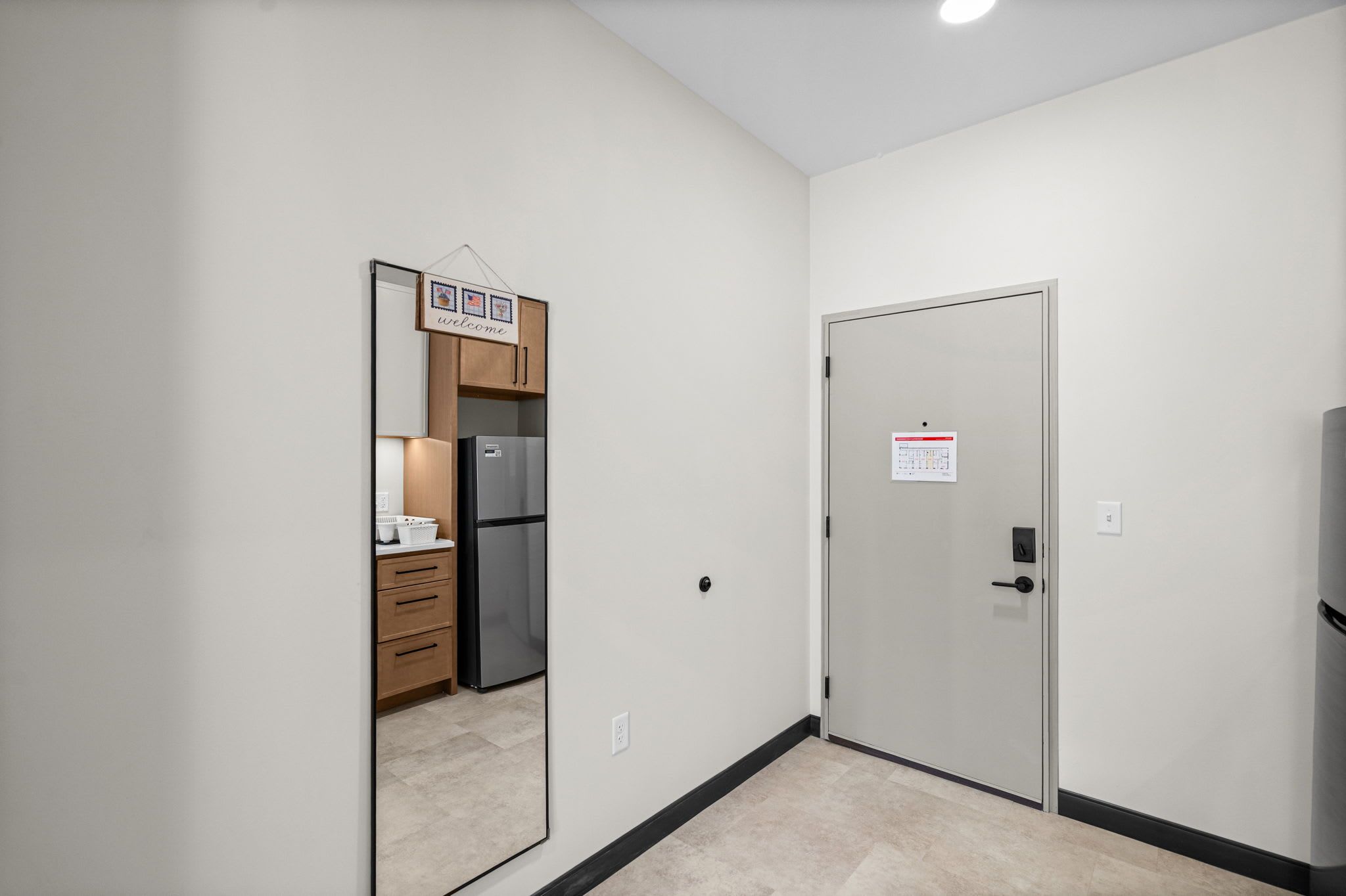A hallway with a door, a refrigerator, and a welcome sign.