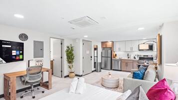 A modern hotel room with a bed, a desk, a chair, a TV, and a kitchenette.