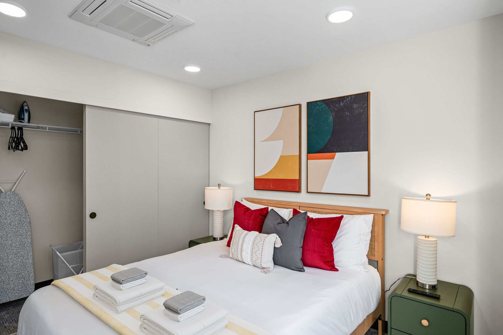 Ein Hotelzimmer mit einem Bett, Kissen, einer Lampe, einem Gemälde und einem Schrank.