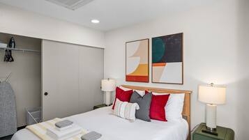 Ein Hotelzimmer mit einem Bett, Kissen, einer Lampe, einem Gemälde und einem Schrank.