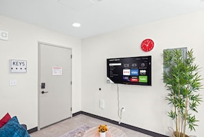 Ein modernes Zimmer mit einem an der Wand montierten Fernseher, der Streaming-Dienste anzeigt, einer Wanduhr und einer Tür mit einem Schild mit der Aufschrift 'KEYS'.