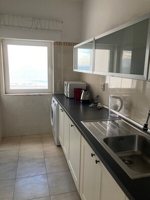 Eine kompakte Küche mit Einbauwaschmaschine, Spüle und Fenster mit Meerblick.