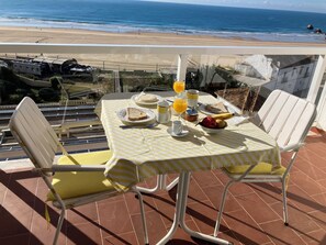 Ein Tisch mit Frühstücksangeboten, einem Glas Orangensaft und Blick auf Strand und Meer.