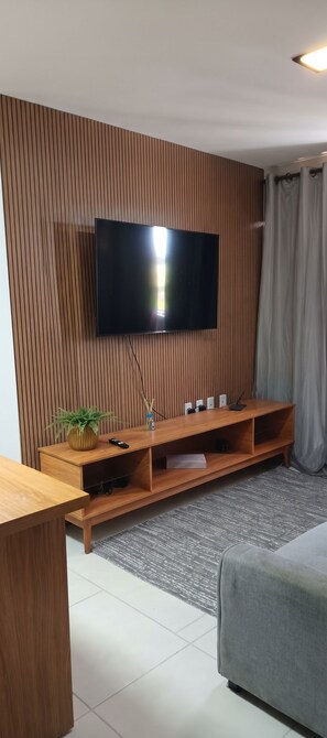 Een moderne woonkamer met een flatscreen televisie die aan een houten wand is bevestigd, een houten dressoir eronder, een grijze bank en een grijs vloerkleed.