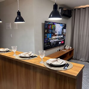 Ein modernes Wohnzimmer mit einem Holzespeisetisch, gedeckt für vier Personen, einem an der Wand befestigten Flachbildfernseher und einer Deckenleuchte.