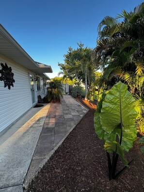 A pathway leading to a white building with a decorative wall piece, surrounded by lush greenery and a well-maintained garden. - Peaceful Palms at Bonita Springs. 10 minutes to the beach and Downtown Shopping (Bonita Springs)