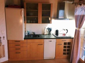 A compact kitchen with wooden cabinets, a built-in dishwasher, and a window with curtains. - Casa Alpetta, (Flumserberg Tannenboden), by Interhome (Flumserberg Tannenheim)