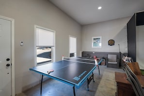 Une table de ping-pong dans une pièce dotée d’une porte, de fenêtres et d’un jeu de fléchettes.