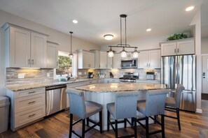 Una cocina moderna con una isla central, taburetes de bar, electrodomésticos de acero inoxidable e iluminación colgante.