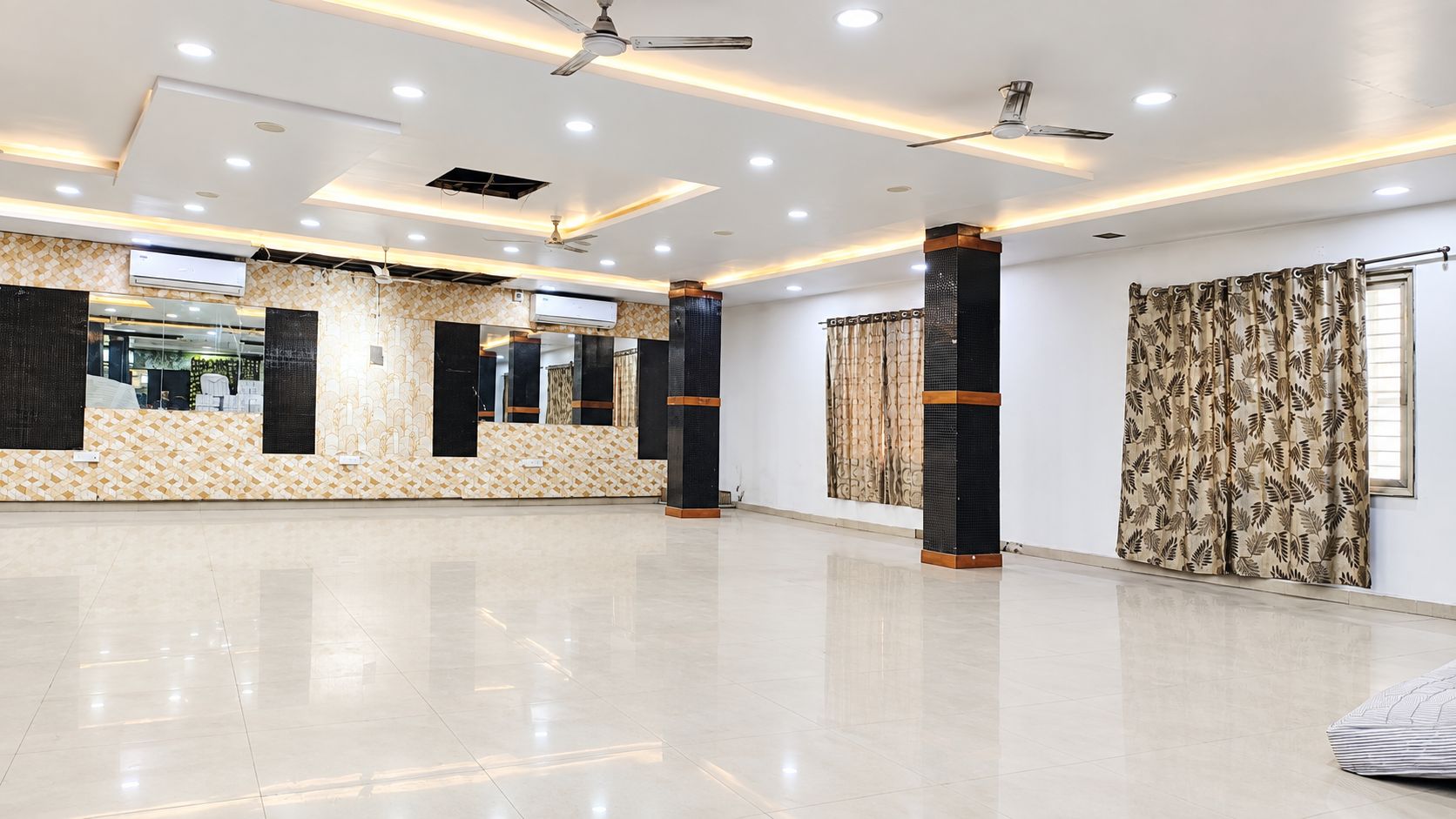 A spacious hotel lobby with a polished floor, ceiling fans, recessed lighting, and a large mirror reflecting the interior.