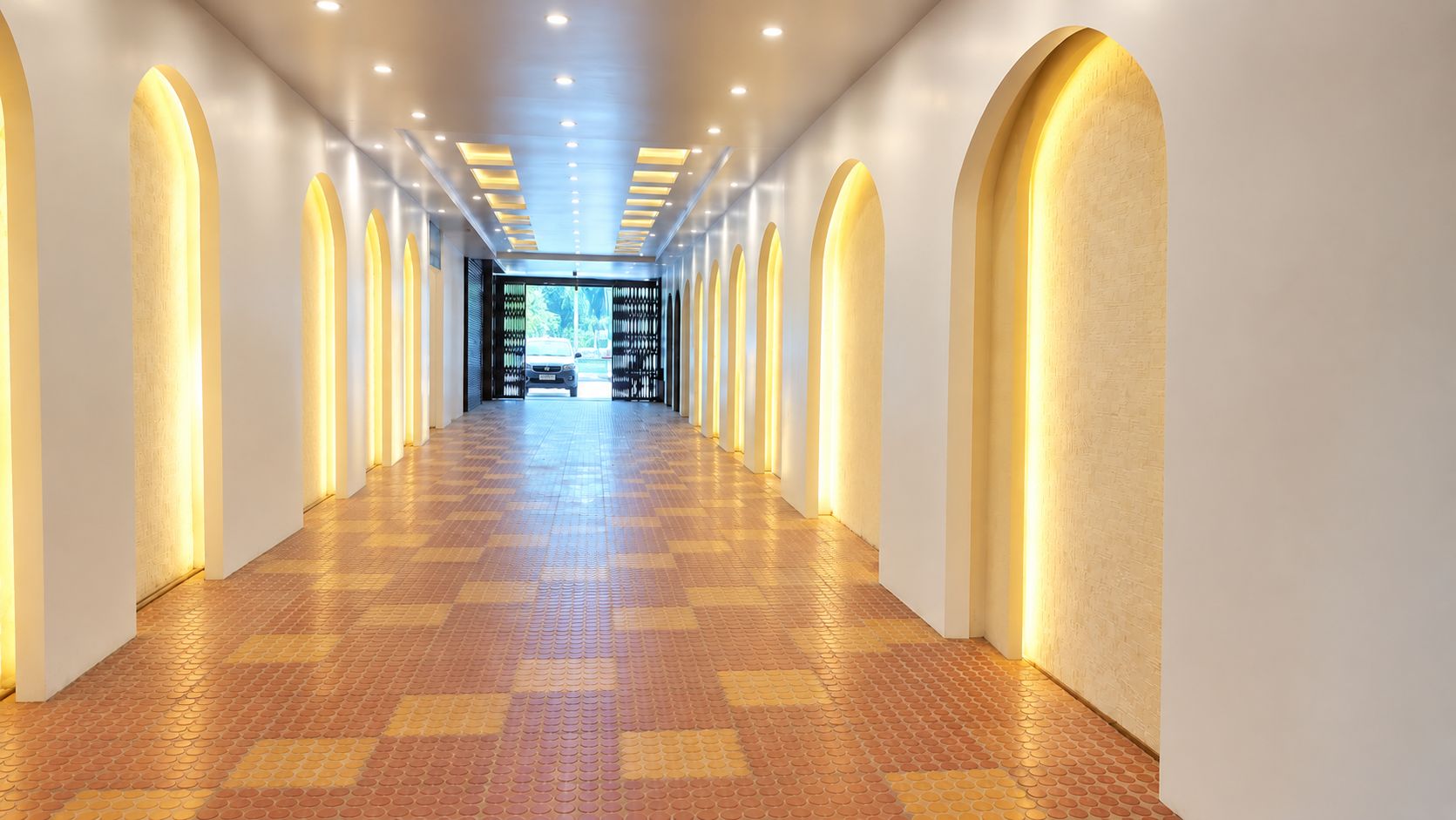 Un largo pasillo bien iluminado con un piso de diseño a cuadros, que conduce a una puerta al final.