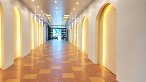 A long, well-lit hallway with a checkered floor pattern, leading to a door at the end.