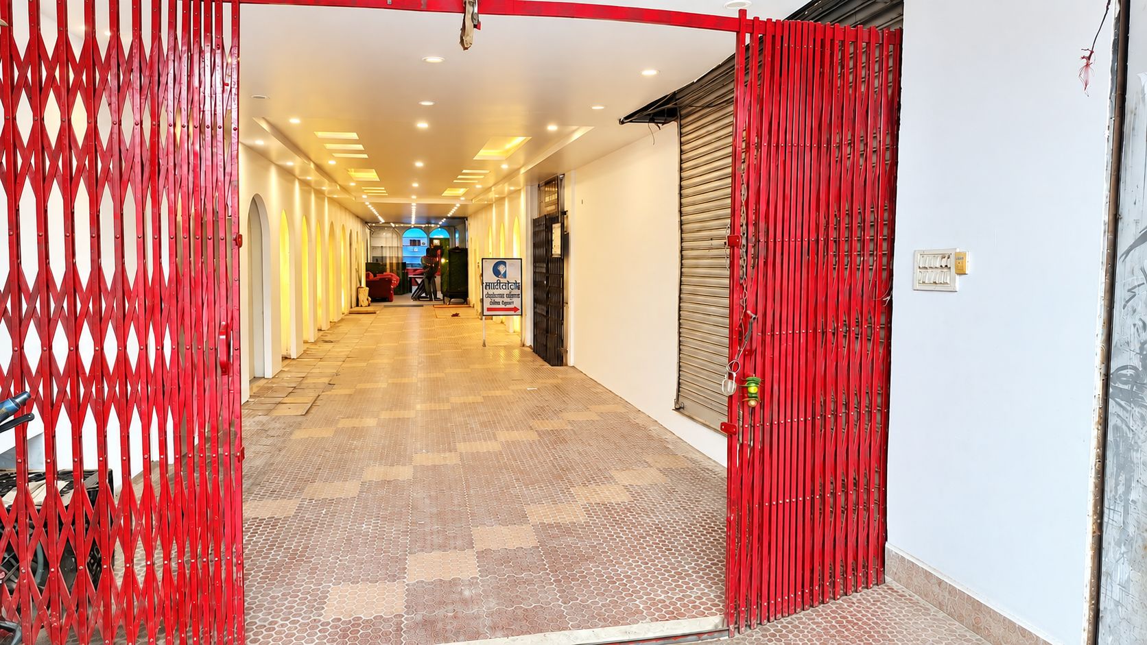 A hotel corridor with a red metal gate, a sign indicating a restaurant, and a tiled floor.