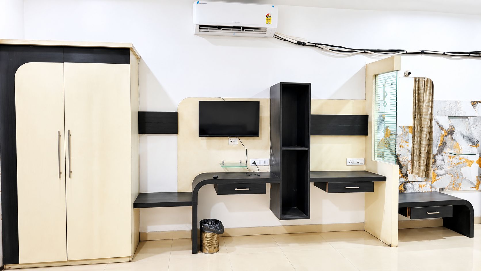 Una habitación con armario, escritorio con computadora, aire acondicionado instalado en la pared y una división de vidrio.