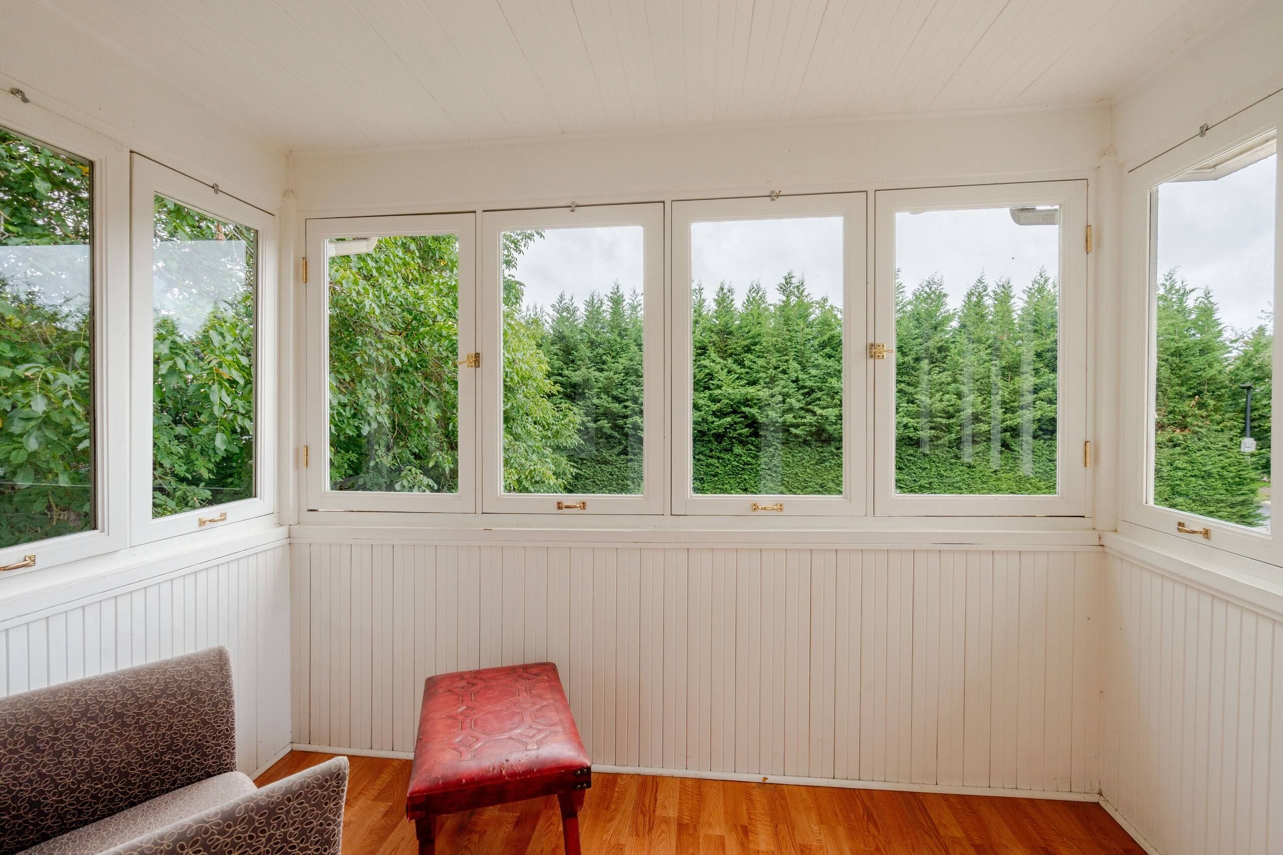 A room with a bench, a chair, and a view of trees through large windows.