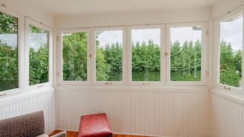 A room with a bench, a chair, and a view of trees through large windows.