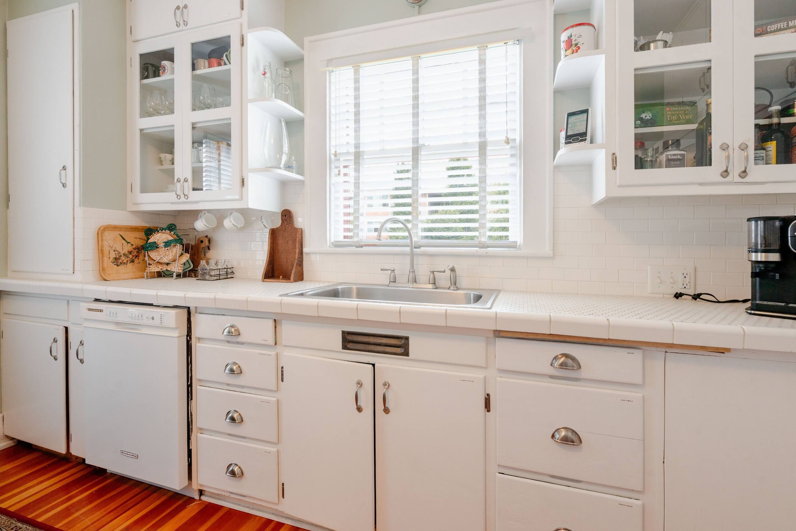 A kitchen with white cabinets, a window with blinds, a sink, and a coffee maker.