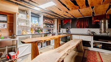A rustic bar area with wooden benches, shelves of bottles, and a large metal container.