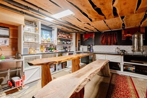 Un coin bar rustique avec des bancs en bois, des étagères remplies de bouteilles et un grand récipient en métal.