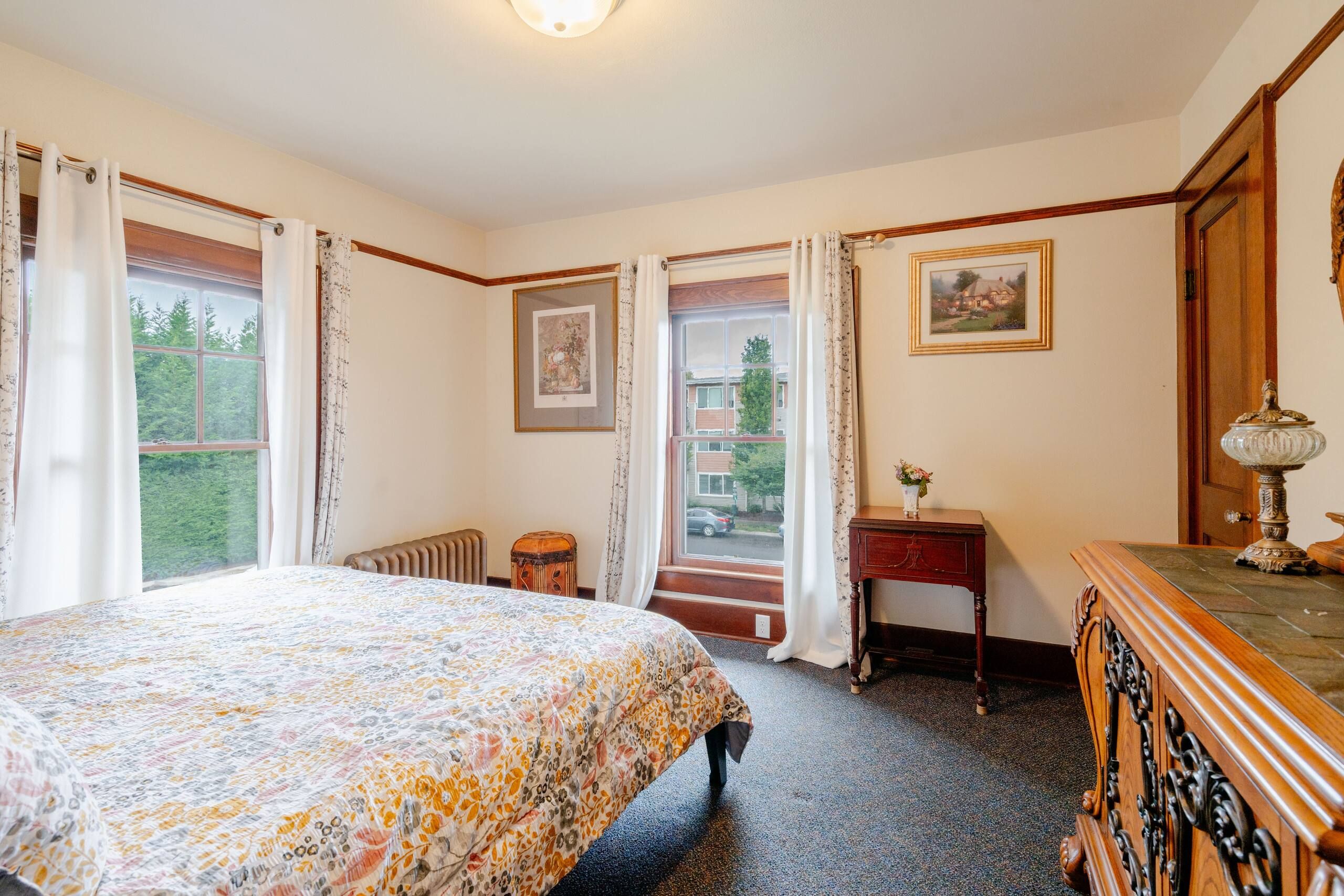 A bedroom with a bed, a dresser, a lamp, and a window with curtains.