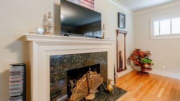 A living room with a fireplace, a television mounted above it, and a bookshelf to the left.