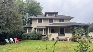 A two-story house with a front porch, a lawn, and outdoor seating.