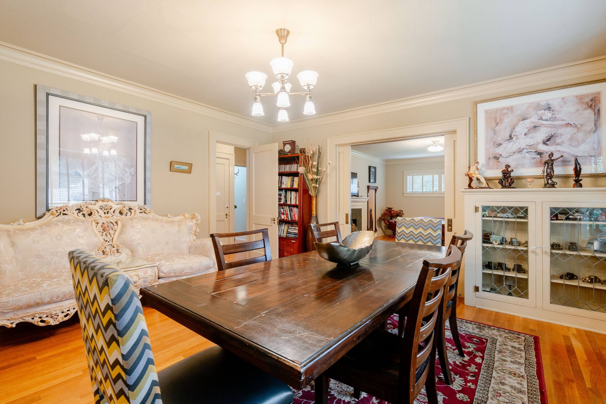 A dining room with a wooden table, chairs, a sofa, and a bookshelf.