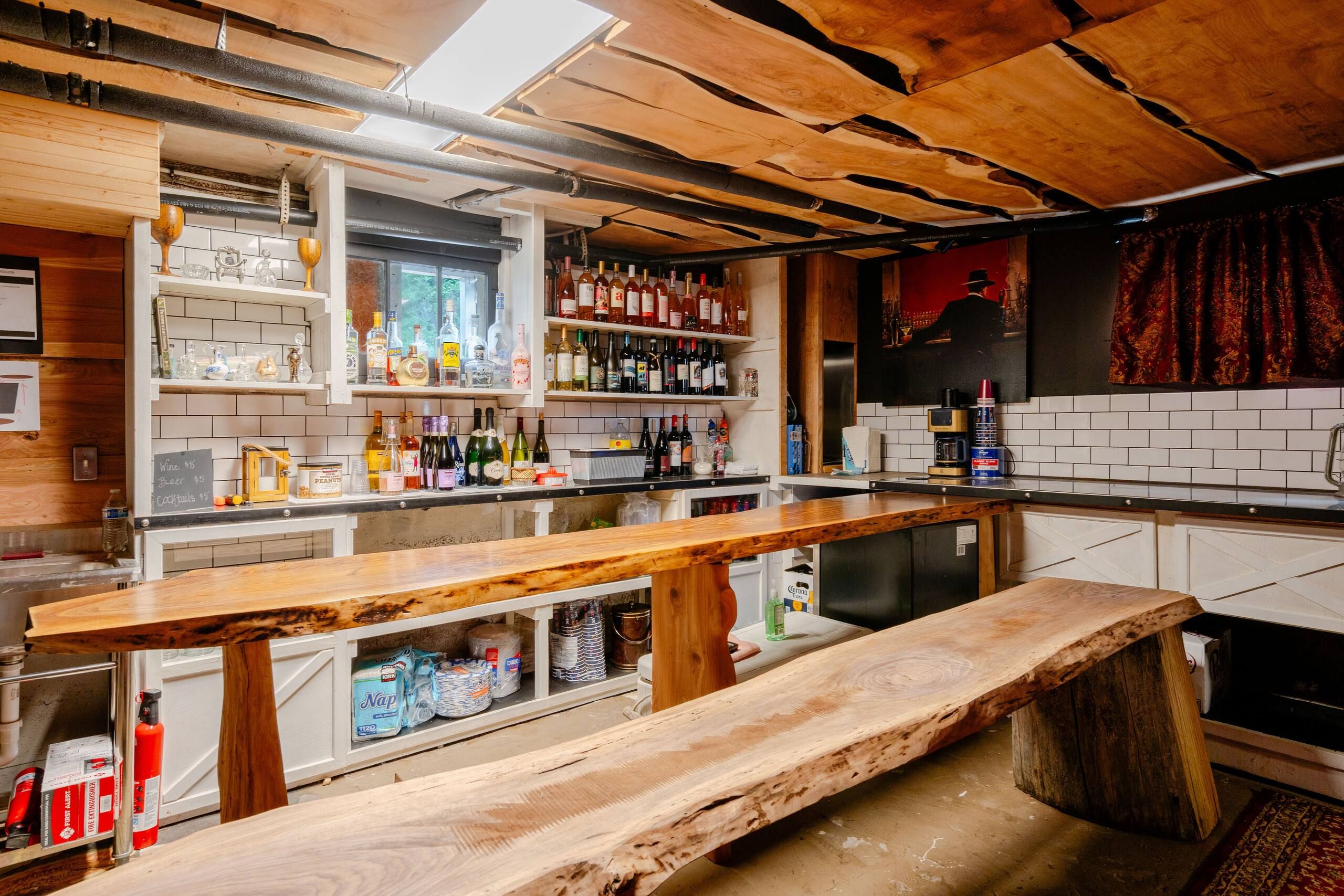 A bar area with wooden bar tops, shelves with bottles, and a chalkboard menu.