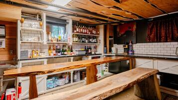 A bar area with wooden bar tops, shelves with bottles, and a chalkboard menu.