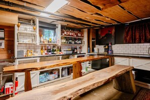 Un espace bar avec un comptoir en bois, des étagères remplies de bouteilles et un menu écrit à la craie.