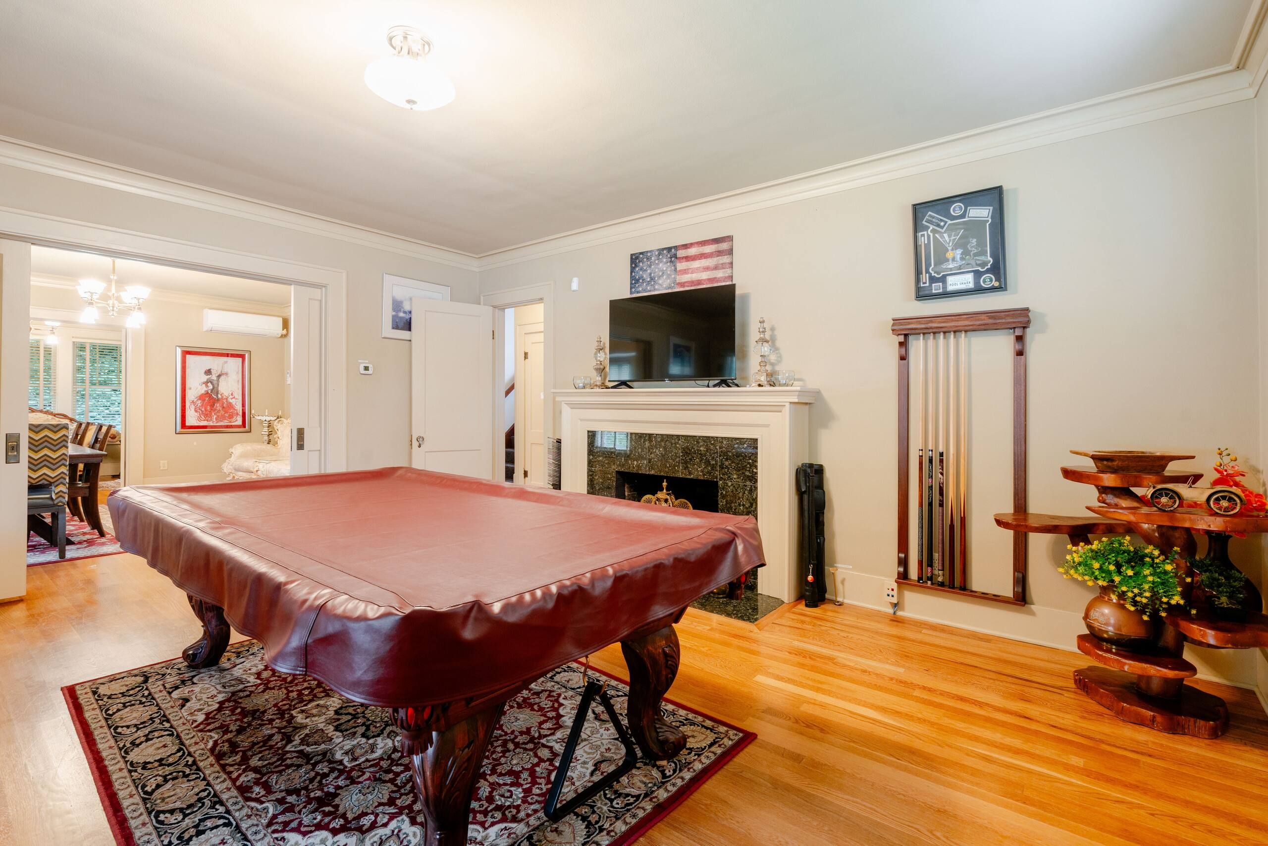 A billiards table in a room with a fireplace, a television above it, and a decorative shelf with toys.