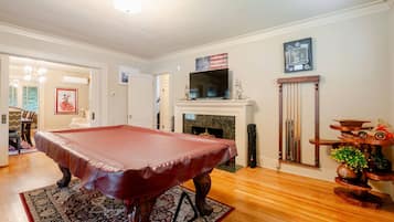 A billiards table in a room with a fireplace, a television above it, and a decorative shelf with toys.