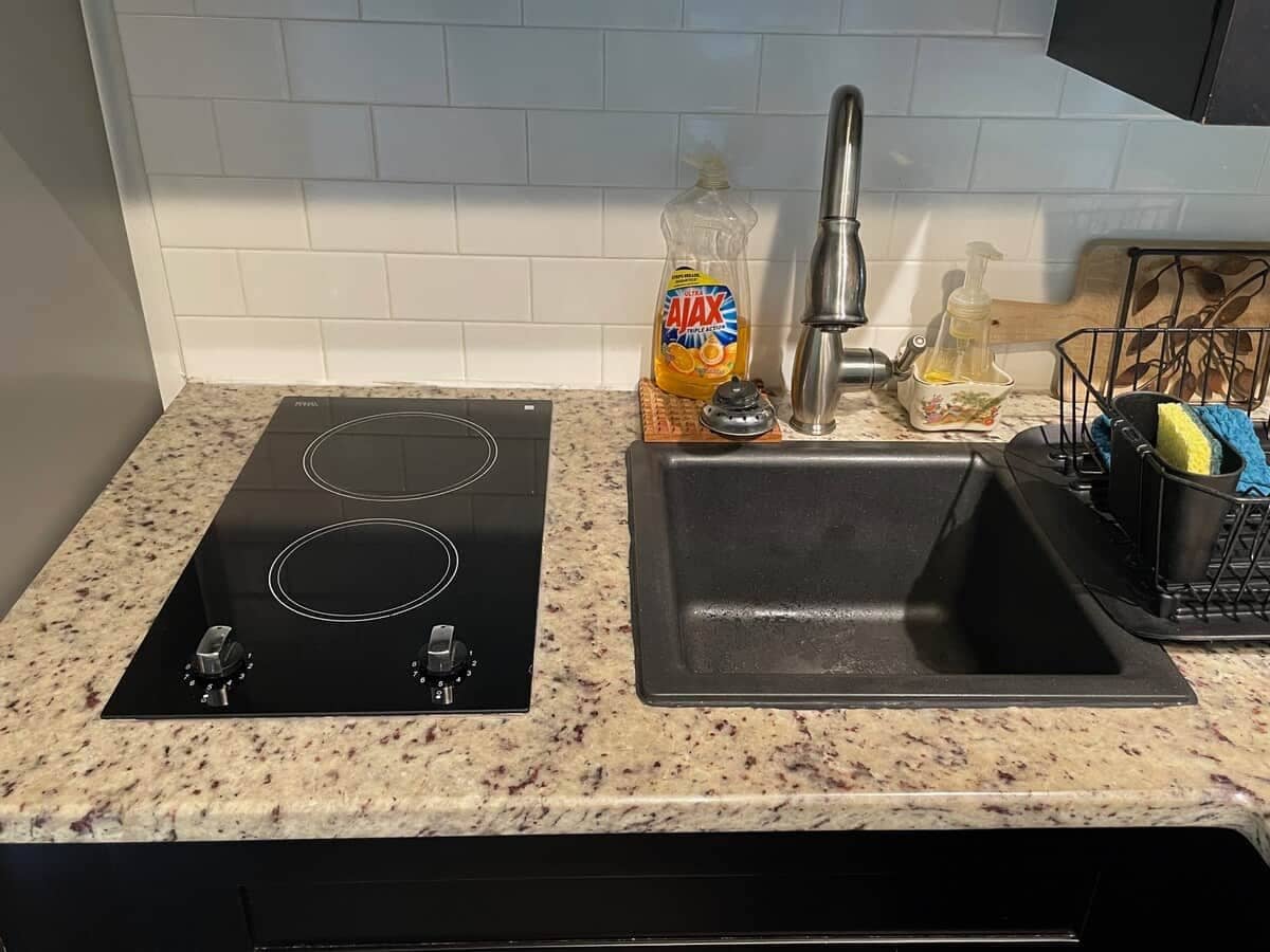 A kitchen with a black induction cooktop, a stainless steel sink, and a bottle of Ajax dish soap.