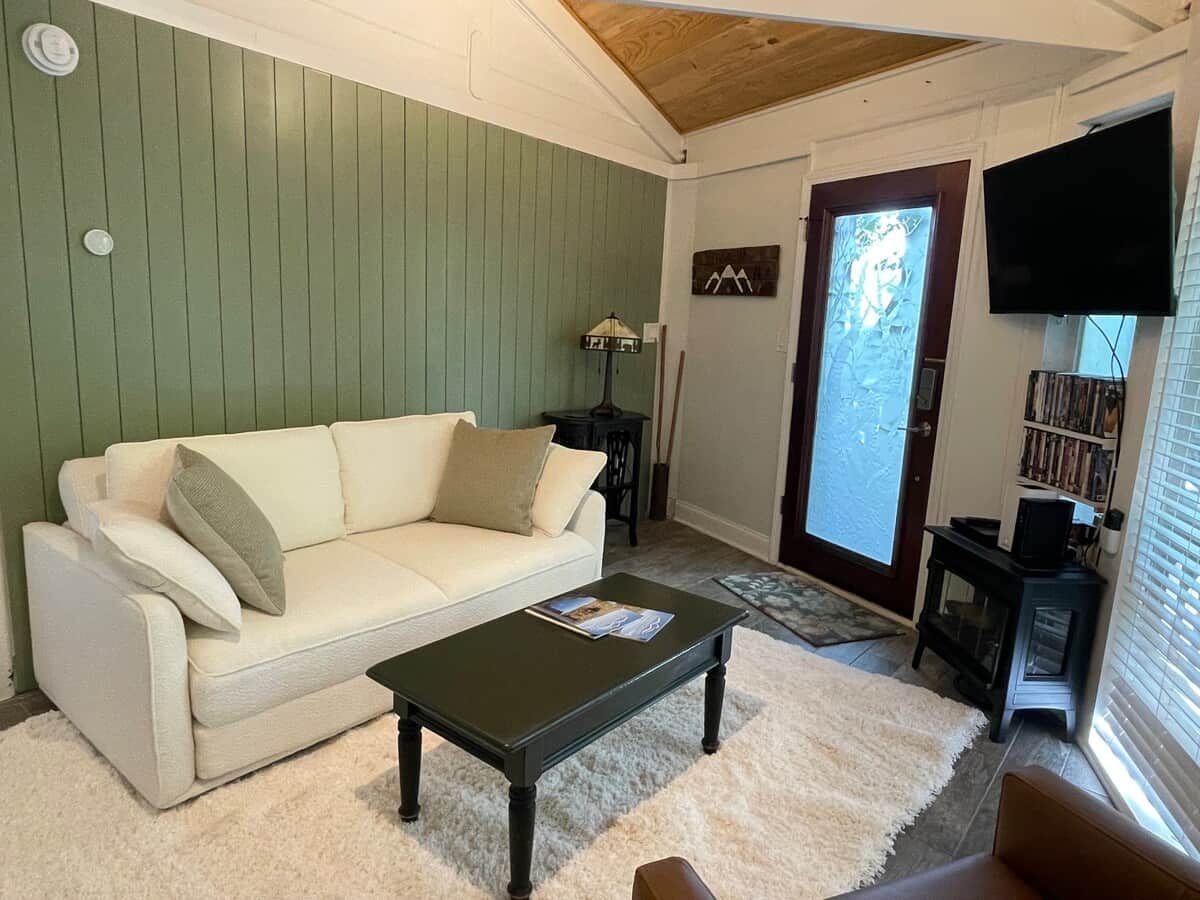 A living room with a white sofa, a dark coffee table, and a television on the wall.