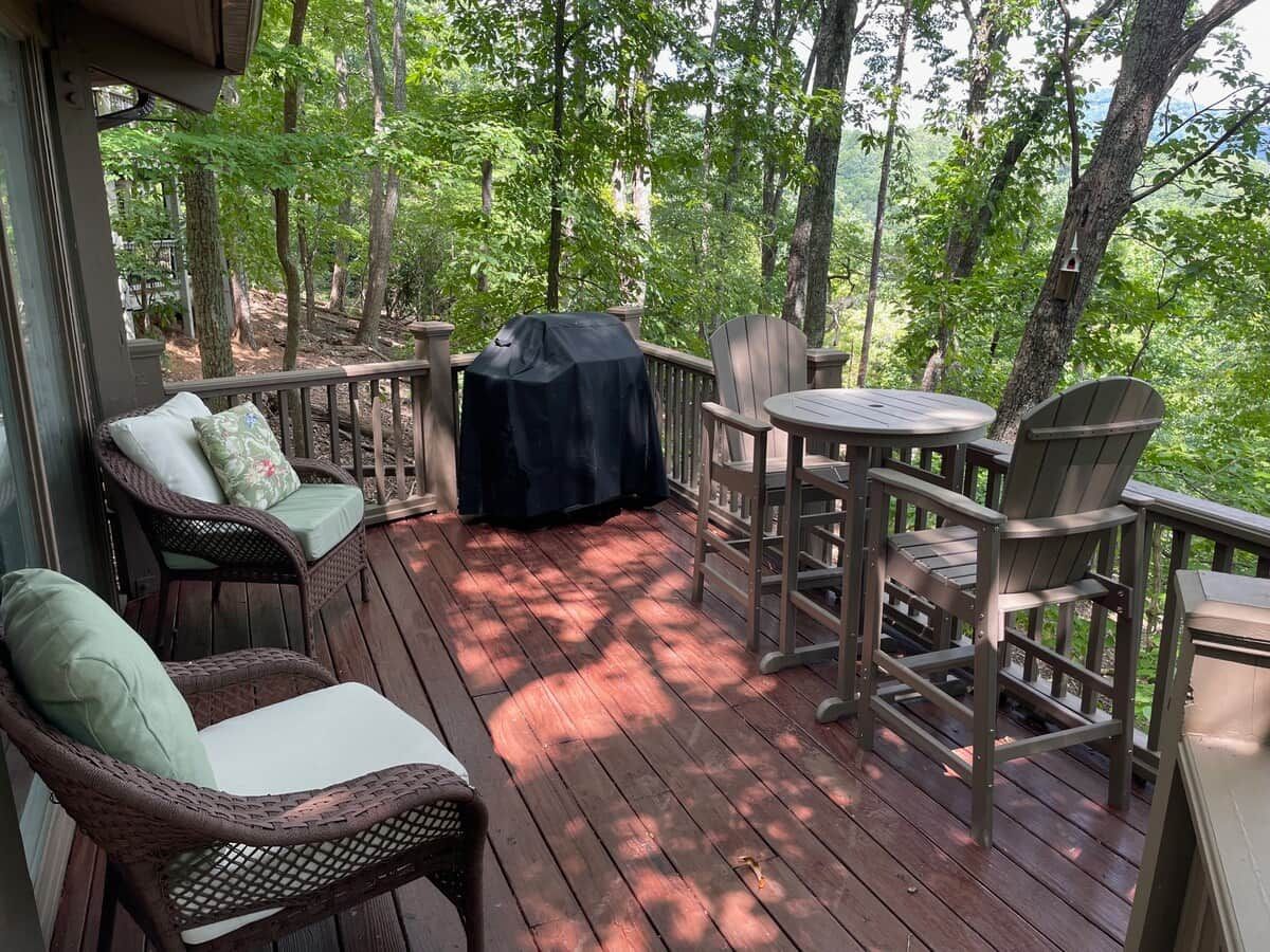 A wooden deck with wicker chairs and a table, surrounded by trees.