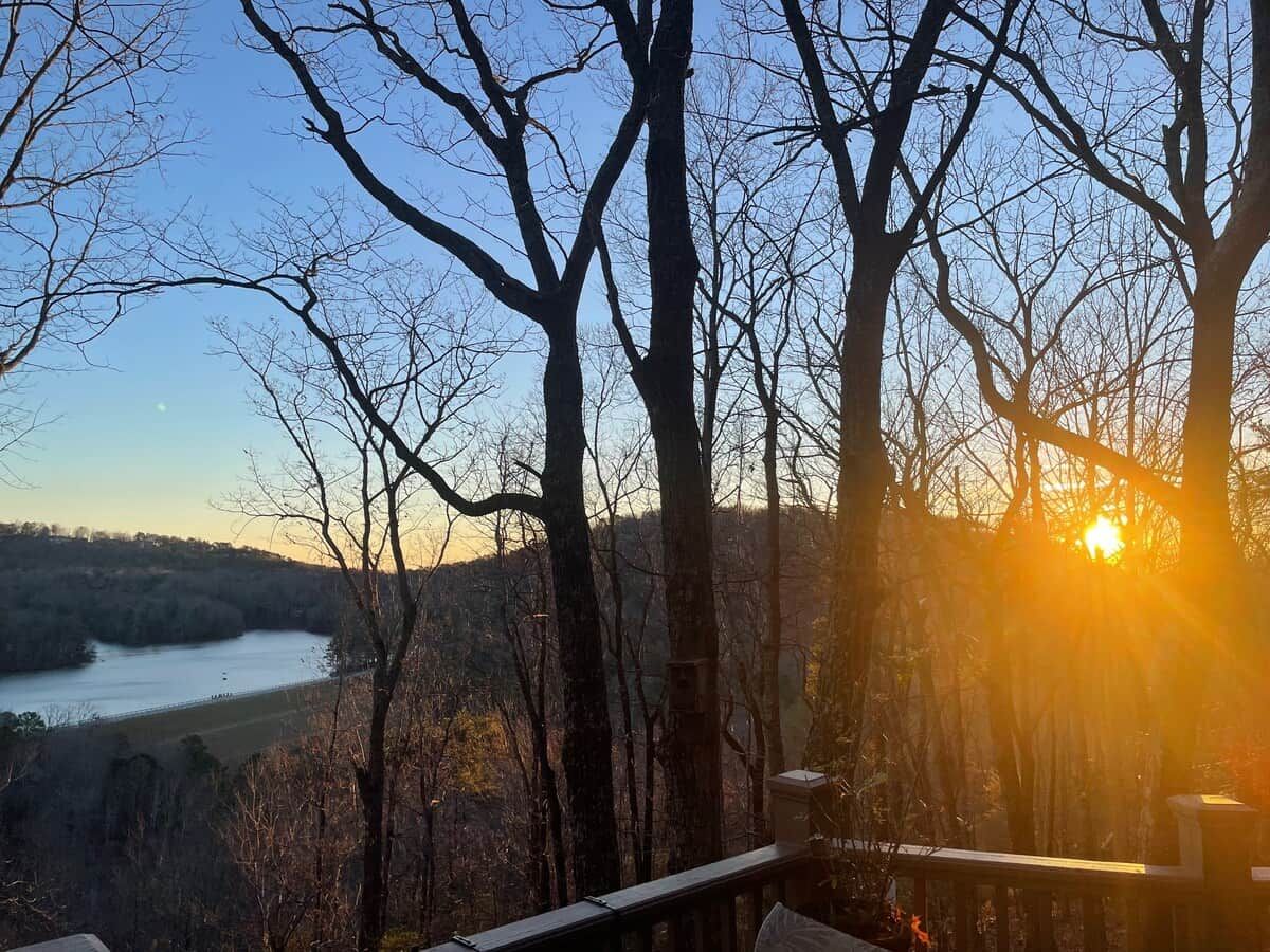 Vista de un río con árboles en primer plano y una puesta de sol al fondo.