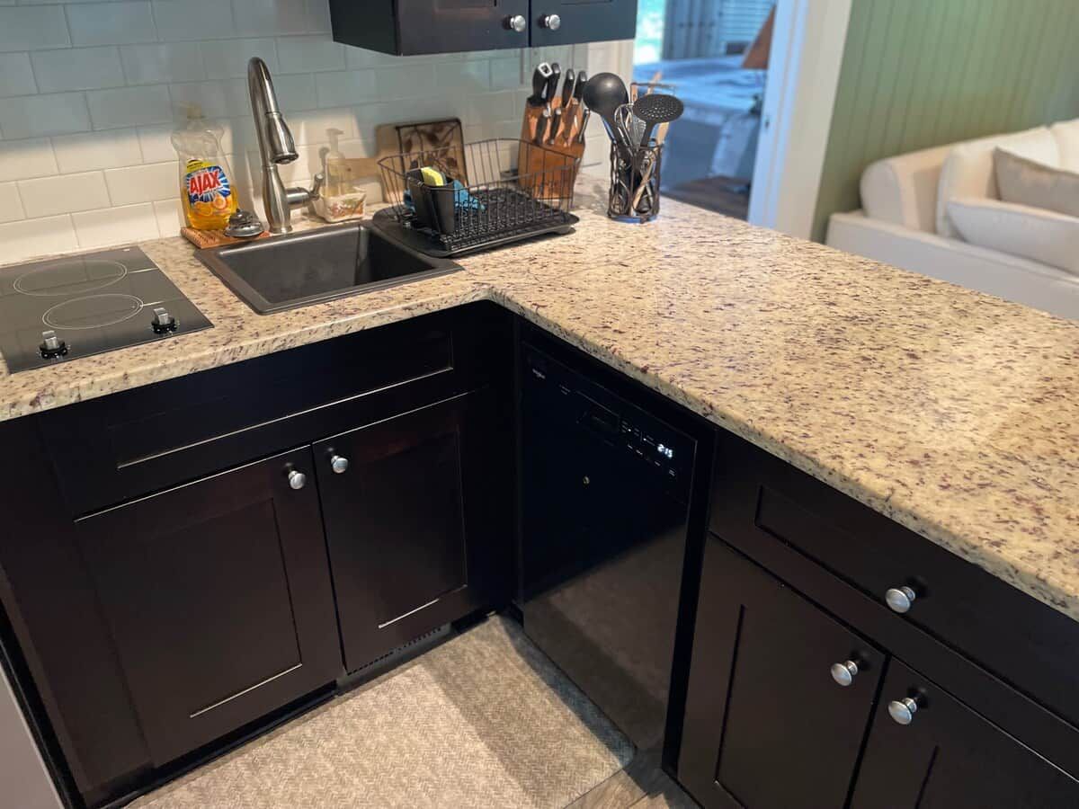 A kitchen with dark cabinetry, a granite countertop, a dishwasher, and a sink.